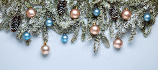 Christmas banner with fir branches and decorations in pastel colors sprinkled with snow. Elegant Christmas border made up of fir branches, beige and blue balls in muted colors