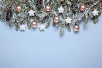 Christmas border with fir branches and decorations in pastel colors, with snow. Elegant Christmas frame from fir branches, beige balls and white stars, in muted colors on a light blue background