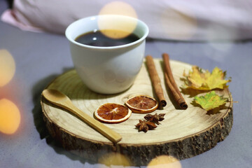 Wooden tray with cup of tea or coffee, wooden spoon, seasonal spices and autumn leaves, served in the bed. Selective focus, prominent bokeh lights.