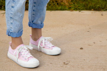 Naklejka premium A view of the legs of a teenage girl in pink sneakers and blue jeans against a background of yellow dry grass. The concept of clothing for modern teenagers, even in the cool season