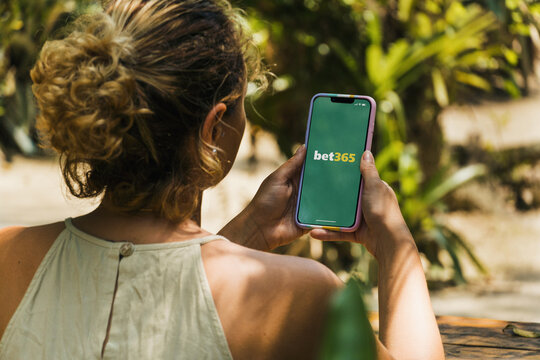 Girl in the park holding a smartphone with Bet365 betting provider app on the screen. Rustic wooden table. Rio de Janeiro, RJ, Brazil. November 2022