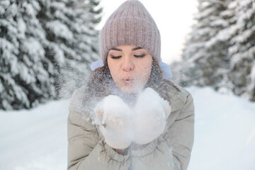 Young beautiful woman blowing snow off the hand.Winter outdoor activity, winter holidays.Selective focus, close up.