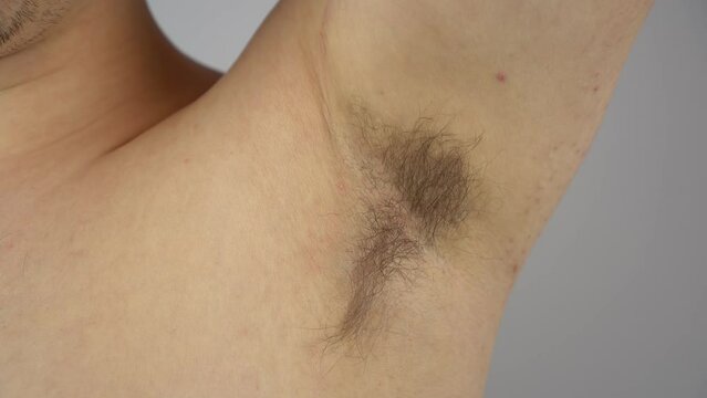 A man raises his hand and shows a hairy armpit on a gray background. Long hair in the armpits. Bodypositive.