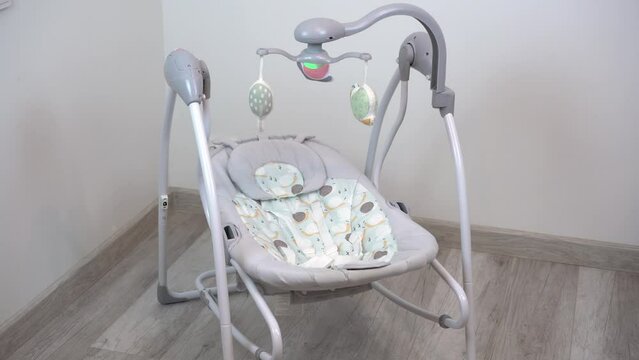 An empty swing-cradle swings in the room. Children's automatic swing for an infant.