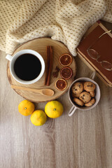 Cup of tea or coffee, various spices, bowl of cookies, tangerines, books, reading glasses and knitted blanket on wooden table. Hygge at home concept, flat lay.