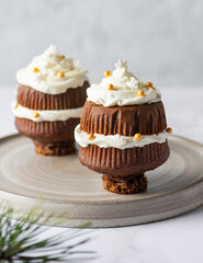 Christmas cupcakes close-up. Chocolate cakes with whipped cream decorated with confectionery sprinkles, sugar gold balls and white snowflakes on a concrete gray background. Winter holiday dessert