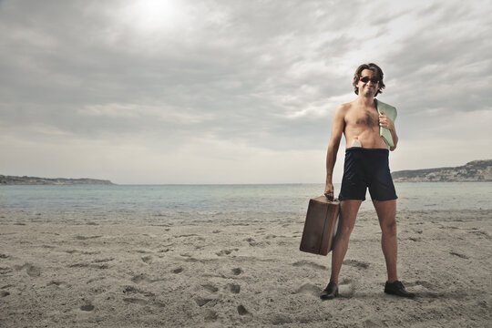 satisfied man in bathing suit with suitcase and sunscreen at the beach