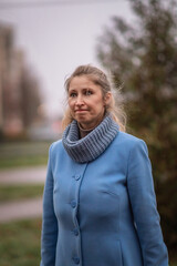 Portrait of a beautiful young fair-haired girl in a blue coat in cloudy weather. There is artistic noise.