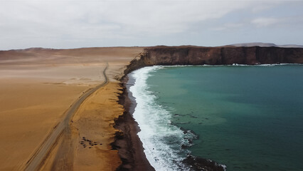 Aerial drone view of the red beach in the Paracas National Reserve, Peru. Beach landscape with sand, road and cliff. Tourism in Peru. Ica desert.