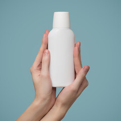 A woman's hands holds a white bottle of shampoo. Template blank copyspace. Blue background.