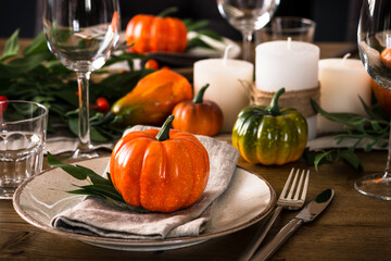 Fototapeta na wymiar Autumn table setting with plate, pumpkin and candles at wooden table. Thanksgiving food festive dinner concept.