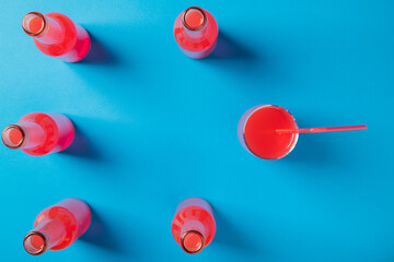 Grapefruit juice in bottles and a glass on a blue background. Pink and red drink on a blue background. Top view.