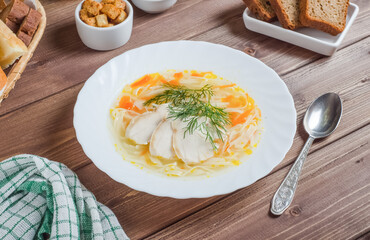Appetizing chicken soup with noodles and pieces of meat in a white plate on a dark wooden background, chef serving