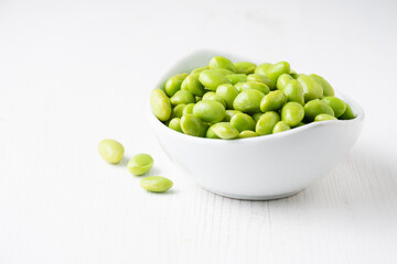 View of white bowl with edamame grains on white wooden table, horizontal, with copy space