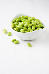 Close-up of white bowl with edamame grains on white wooden table, vertical, with copy space