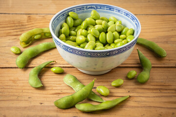 Top view of edamame beans in blue chinese bowl, on wooden table with pods, horizontal