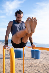 Front view of brunette man practicing calisthenics on parallel bars. Sports concept.