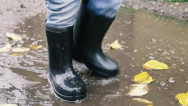 child in rubber boots stomps in a puddle, mud splashes. slow motion video