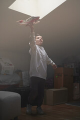 Preteen boy playing with a toy airplane pretending to fly in the attic of his home. Daydreaming...