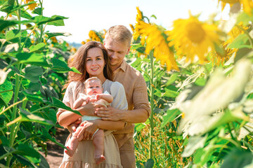 Fototapeta premium A young family with a little cute baby in a field of sunflowers. Happy summer, Family activities and outdoors lifestyle.