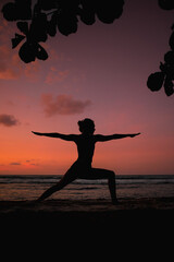 silhouette of a woman practicing a yoga posture (warrior 2) during sunset on the beach. Beach landscape in Costa Rica. Sports, wellness and spirituality.