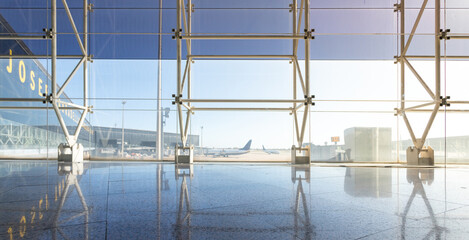 Views of the airstrip and fingers with planes from inside an airport. Curtain wall-type metal structure with tinted glass. Planes and runway in the background.