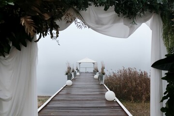 Romantic scenery with a wooden pier with white gazebo and plants in white flower pots, and white...