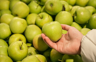 Close-up, an apple in a woman's hand, a selection of fruits in a supermarket.
