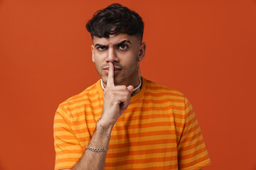 Brunette young man frowning while showing silence gesture