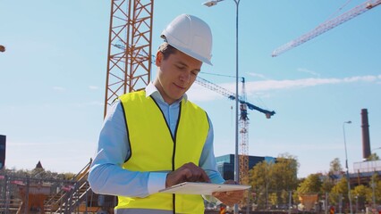 Professional builder standing in front of construction site. Foreman in hardhat helmet and vest. Office building and crane background. Business, real estate and investment.