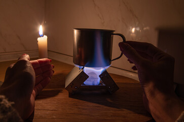 A small tourist pocket stove with fuel tablets for heating water for food in a metal mug in darkness during a power and gas outage at home. Blackout, load shedding, power outage, energy crisis.