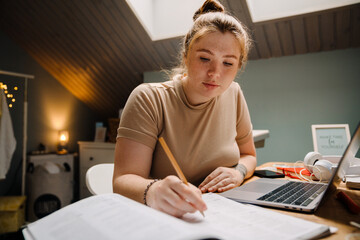 Young beautiful focused girl doing homework writing with pencil