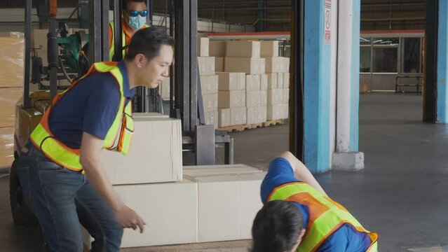 Worker lift box and accident with injured while colleagues to help in the warehouse at factory, first aid and emergency, safety and security, medical assistance, industrial and insurance concept.