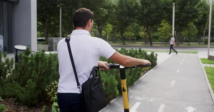 Rear view of businessman walking with electric scooter. Male professional commuting on street in city. He is wearing formals.