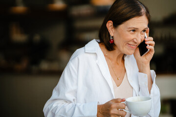 White mature woman drinking coffee and using cellphone in cafe