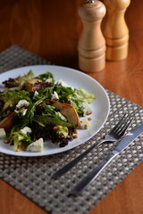 meat and pear salad on a white plate with cutlery against the background of salt and pepper