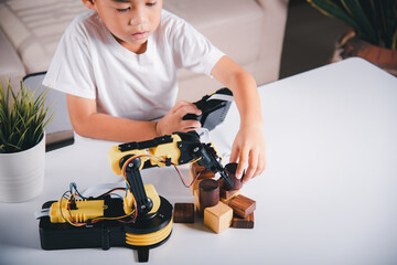 Happy Asian little boy using remote control playing robotic machine arm for pick up wood block,...