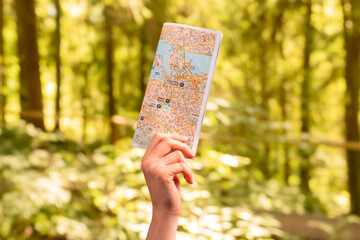 Sport orienteeing concept. Paper map, guide in hand on blurred forest nature background. Navigation, orientation