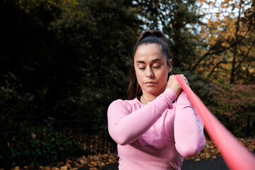 Sport woman with eyes closed is using a resistance band in a park.
