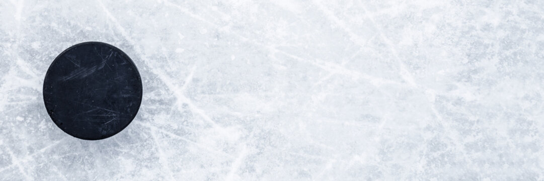 Black old rubber puck on ice background. Closeup. Wide banner. Top down view. Empty place for text.