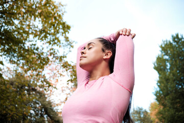 Portrait of fitness woman stretching with eyes closed. She is is in a park.