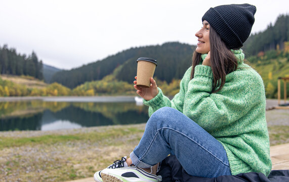A young woman with a cup of coffee on a blurred background of mountains.