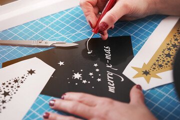 christmas graphic cut from black adhesive foil is finished by female hands with painted nails....