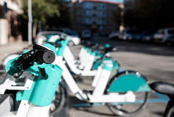 Plakat Rental e-bikes are parked in a row at the dock station in a city.