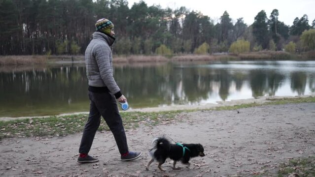 Bearded man in funny hat on autumn walk with dog in evening forest.