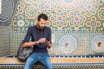 Young Muslim man using a mobile phone in front of traditional arabesque mosaic
