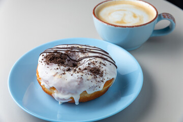 Donut covered with icing sugar and chocolate powder on blue plate and cup of cappuccino