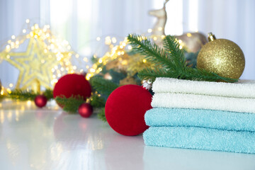 Stack of blue and white towels folded on the table, fir branches, Christmas balls and Christmas lights. SPA massage or beauty salon, relaxation and self care in Christmas or New Year variant.