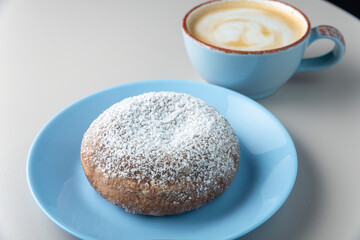 Donut covered with sugar powder on blue plate and cup of cappuccino