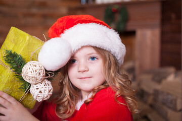 Beautiful little blonde baby girl, has happy fun cheerful smiling face, blue eyes, dressed in red Christmas Santa suit. Kids holiday fashion. Close up. Winter background. Family portrait.